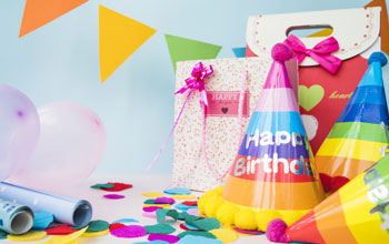 Table with party hat, gift bag, wrapping paper, balloons and confetti. 