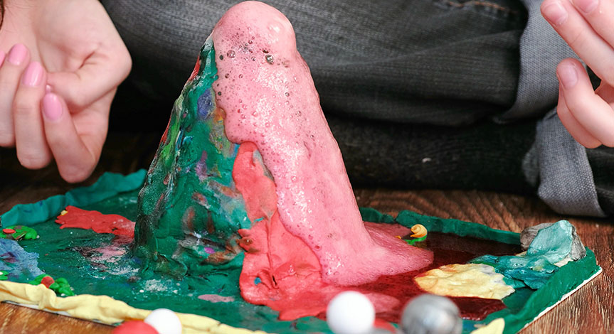 Kids hands make volcano on wood floor. Chemical reaction causing red liquid to overflow.